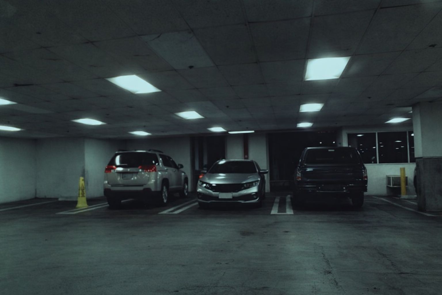 Tre bilar parkerade i ett mörkt, underjordiskt parkeringsgarage med lysrör i taket.
